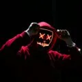 A spooky illuminated mask figure with a red hoodie in a dark setting, perfect for Halloween themes.