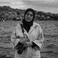 Black and white portrait of a woman standing by the sea holding a camera.