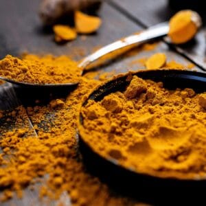 Close-up of vibrant turmeric powder with root on rustic wooden table, emphasizing texture and color.