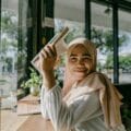 A smiling woman in a hijab reading a book by a window in a cozy cafe in Banda Aceh, Indonesia.