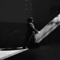 Black and white image of a woman in a hijab walking through a sunlit alley.