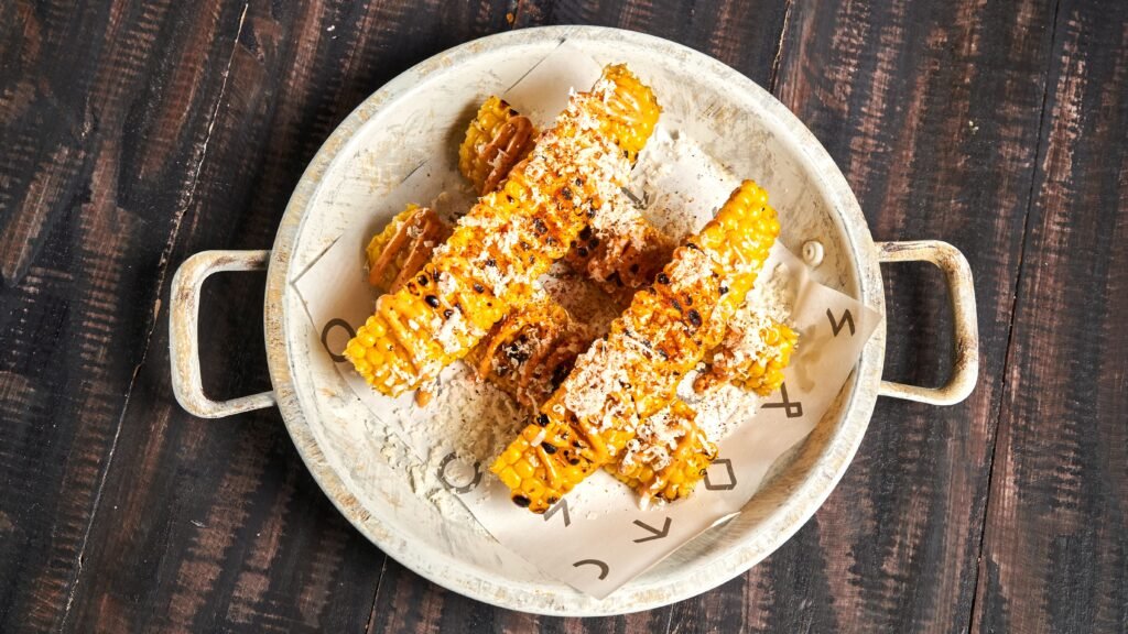Corn ribs jagung panggang dengan taburan bumbu dan keju di piring rustic