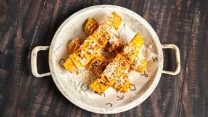 Corn ribs jagung panggang dengan taburan bumbu dan keju di piring rustic